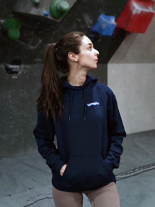 Femme de face dans une salle de bloc portant le sweat à capuche bleu marine Bloc après bloc, jusqu'au sommet
