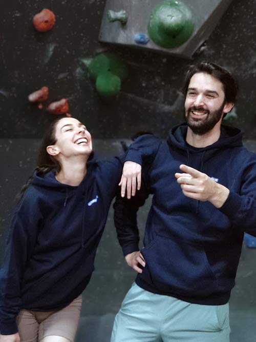 Femme et homme de face dans une salle de bloc portant le sweat à capuche bleu marine Grimpeur de blocs, maître des hauteurs