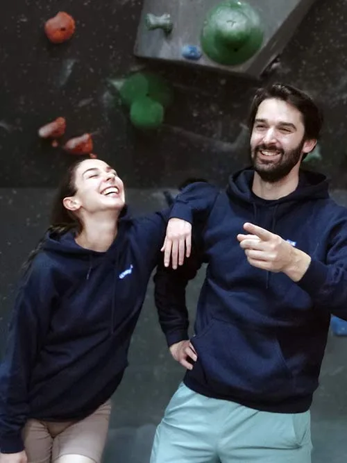 Femme et homme de face dans une salle de bloc portant le sweat à capuche bleu marine Grimpeur de blocs, maître des hauteurs