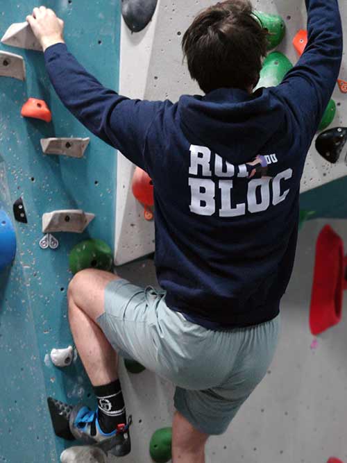 Homme de dos en train de grimper sur un mur de bloc avec le sweat à capuche bleu marine Roi du bloc