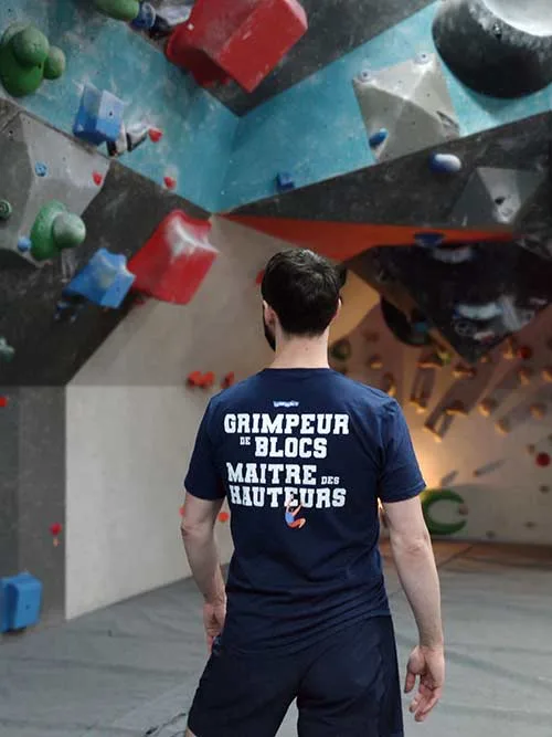Homme de dos dans une salle de bloc portant le t-shirt bleu marine Grimpeur de blocs, maître des hauteurs