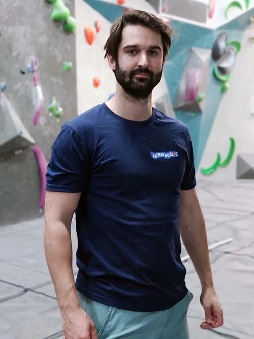 Homme de face dans une salle de bloc portant le t-shirt bleu marine Grimpeur de blocs, maître des hauteurs