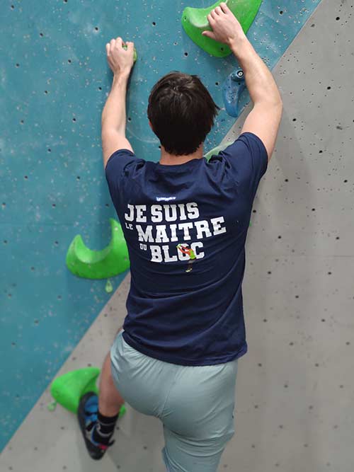 Homme de dos en train de grimper sur un mur de bloc avec le t-shirt bleu marine Je suis le maître du bloc