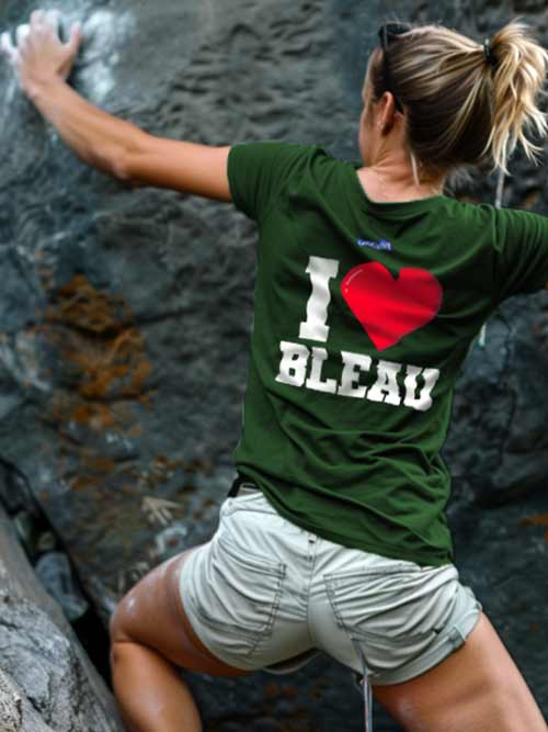 Femme de dos grimpant un rocher en forêt de Fontainebleau, portant le t-shirt vert forêt I love Bleau