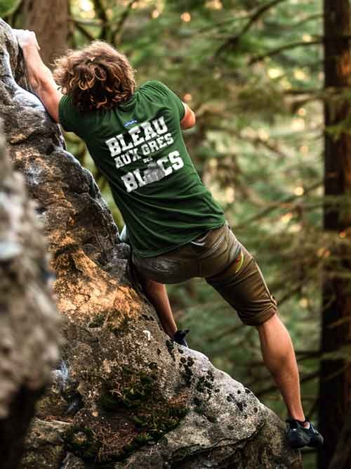 Homme de dos grimpant un rocher en forĂȘt de Fontainebleau, portant le t-shirt vert forĂȘt Bleau aux GrĂšs des Blocs