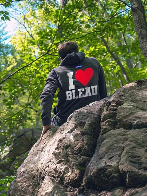 Homme de dos grimpant un rocher en forêt de Fontainebleau, portant le sweat à capuche gris foncé I love Bleau