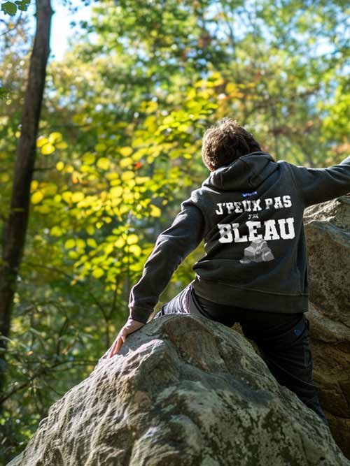 Homme de dos grimpant un rocher en forêt de Fontainebleau, portant le sweat à capuche gris foncé J’peux pas, J’ai Bleau