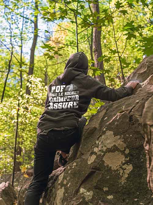 Homme de dos grimpant un rocher en forêt de Fontainebleau, portant le sweat à capuche gris foncé Pof sur le rocher, Grimpeur assuré