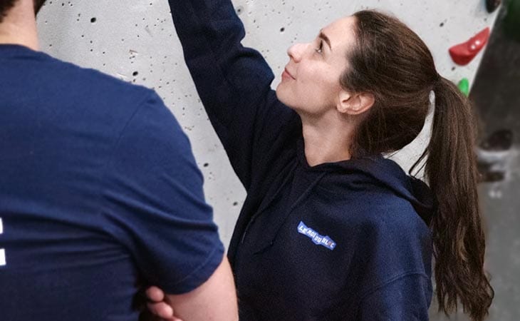 Homme de dos et femme de profil dans une salle de bloc portant un sweat à capuche bleu marine Le Roi du Bloc
