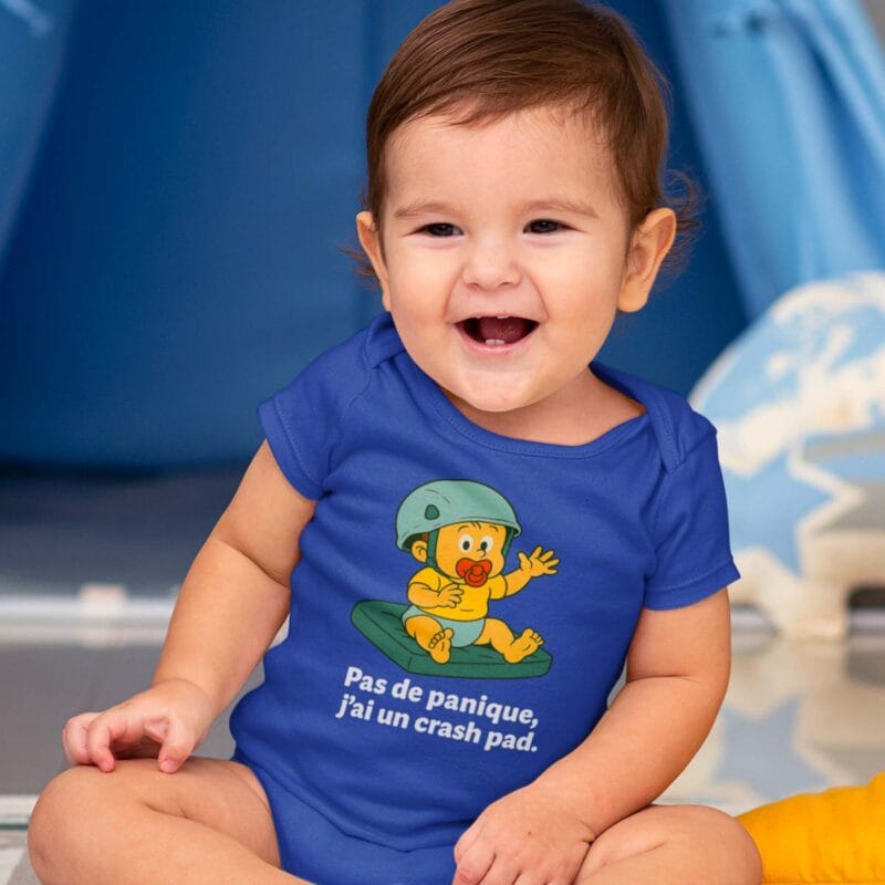 Bébé assis portant le body bleu "Pas de panique, j'ai un crash pad"
